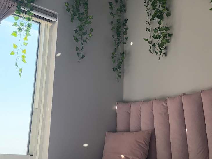 A bed with a pink head board and decorative ivy hangs down.