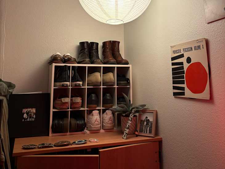 Shoe organizer with various shoes, framed photos, a plant, and a decorative wall art piece in a cozy corner.