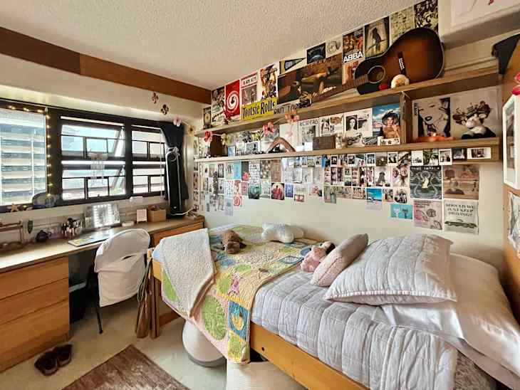 Neatly made twin bed in dorm room with collage on wall.