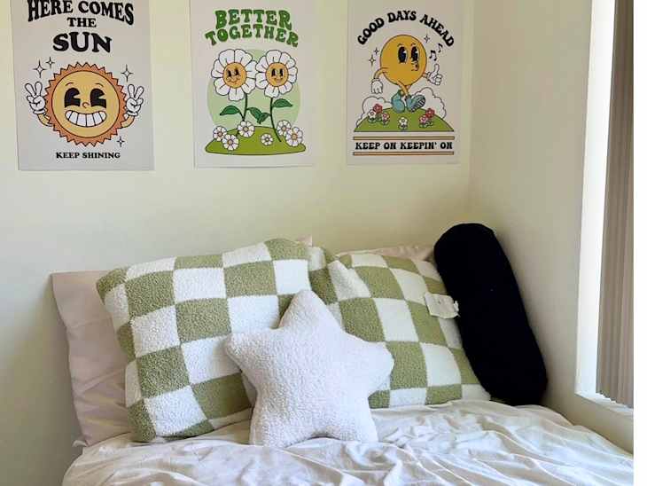 Cozy bed with green and white checkered pillows, a star-shaped pillow, and cheerful wall art featuring sun and flowers.