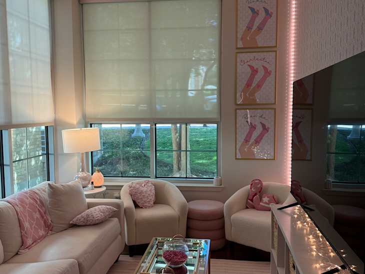 Cozy living room with a light pink sofa, two armchairs, a glass coffee table, and decorative art on the walls.