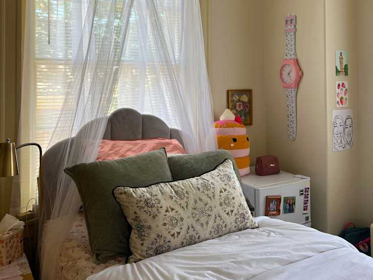 Cozy bedroom with a gray upholstered bed, decorative pillows, a large wall clock, and a plush dessert toy.