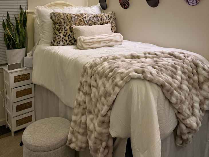 Cozy bedroom with a white bedspread, leopard print pillows, a plush throw blanket, and a potted plant beside a nightstand.