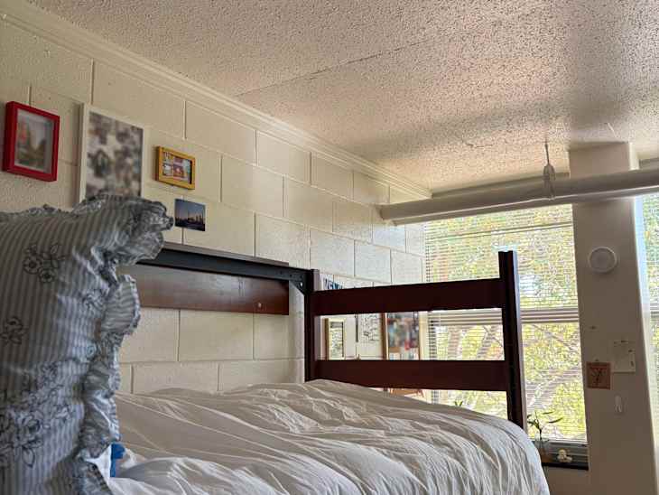 Bunk bed with white bedding, blue striped pillow, and wall decor in a bright room with a window.