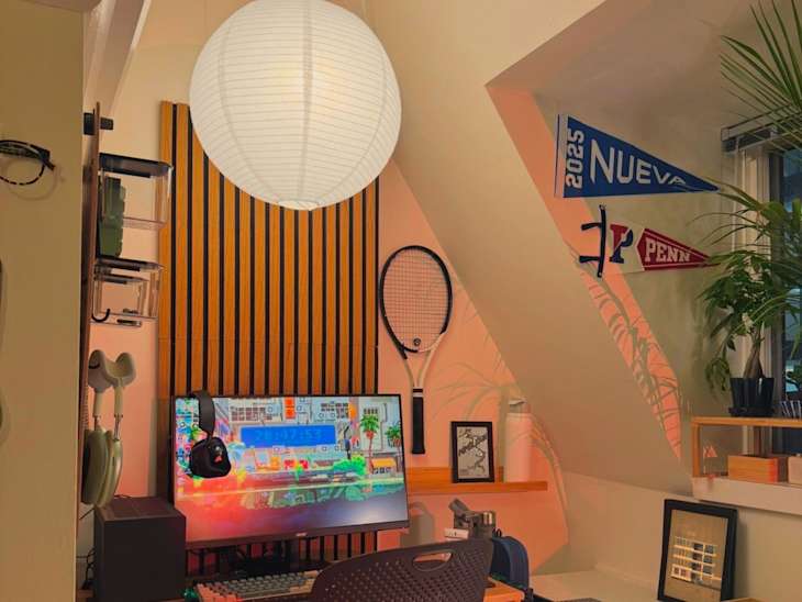 Cozy workspace with a computer monitor, headphones, tennis racket, and decorative pennants on the wall.