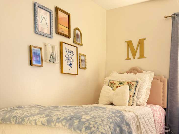Cozy bedroom corner featuring a pink bed with decorative pillows, a blue throw blanket, and a gallery wall of framed art.