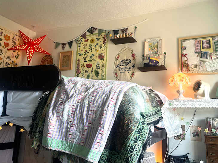 Cozy bedroom with a lofted bed draped in colorful quilts, a star-shaped lamp, floral wall art, and decorative shelves.