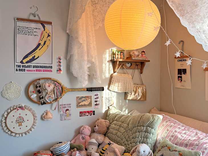 Cozy bedroom corner with a green quilted bedspread, plush toys, a paper lantern, and vintage decor on the walls.