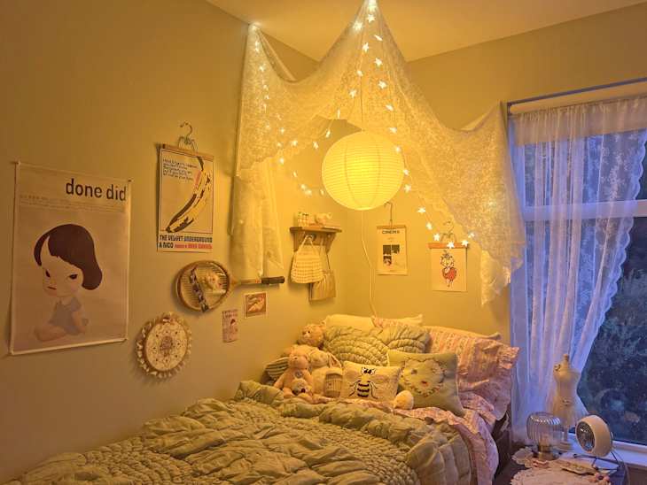 Cozy bedroom with a bed covered in a green quilt, fairy lights, wall art, and plush toys.