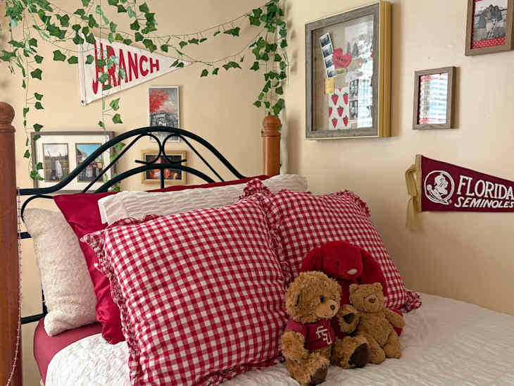Cozy bedroom with a bed featuring red gingham pillows, stuffed animals, and ivy decor on the walls.