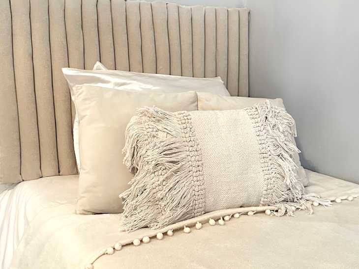 Neatly made bed with painted pool noodle headboard.