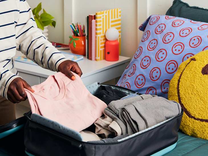 person slightly taking out a pink shirt from suitcase that's on top of a bed with teal sheets