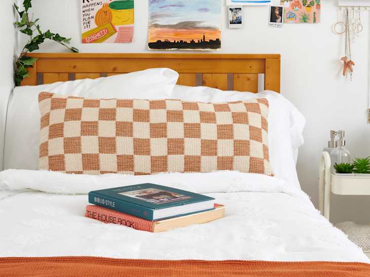 closeup shot of books on a bed with checkered orange and cream pillow behind it - photo gallery wall behind headboard
