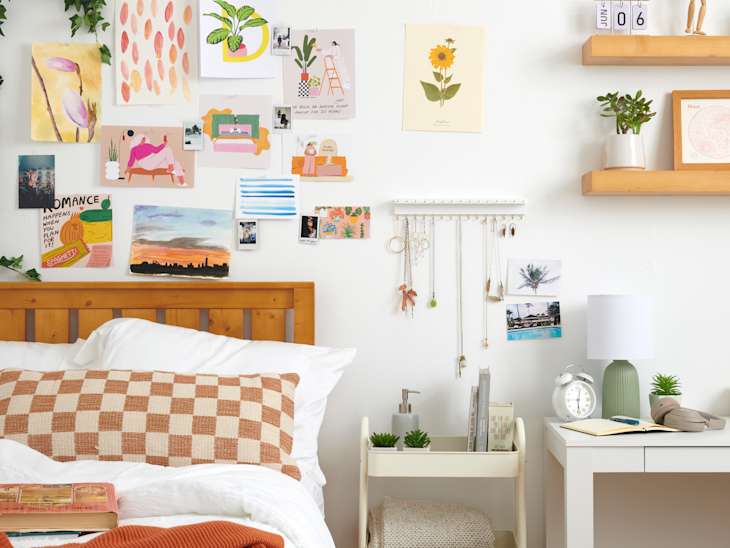 forward shot of bedroom with books on the bed, a desk with items on it and a wall filled with photos, jewelry organizer and a wall shelf