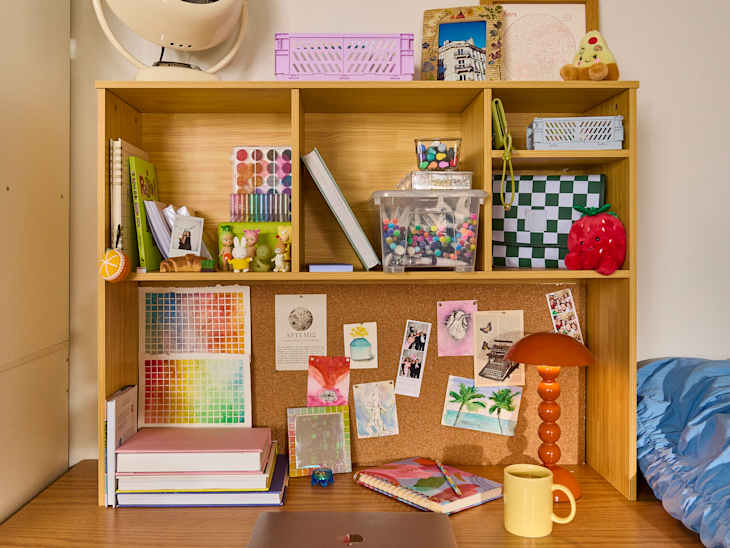 A wooden desk organizer filled with art supplies, photos, and decor, featuring a colorful lamp and a yellow mug.