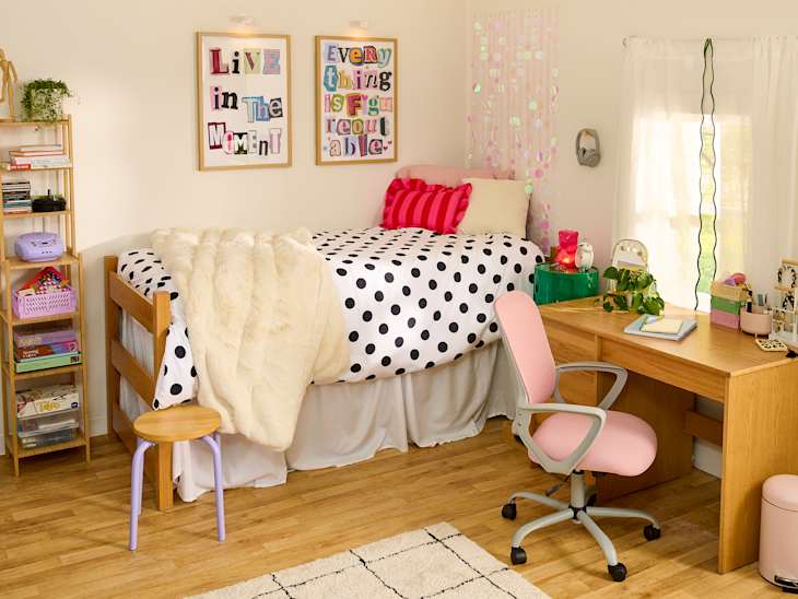 Cozy bedroom with a lofted bed, polka dot bedding, a pink desk chair, and colorful decor items on a wooden desk.