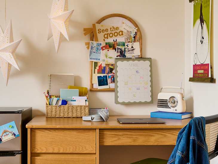 A wooden desk with a laptop, a vintage radio, a calendar, and a basket of stationery. Two star-shaped lights hang above.