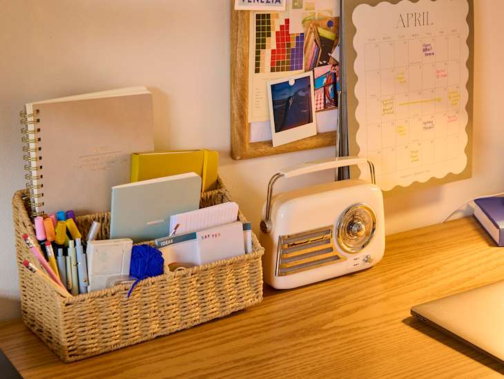 Desk with a woven basket of colorful stationery, a vintage radio, and a calendar for April on the wall.