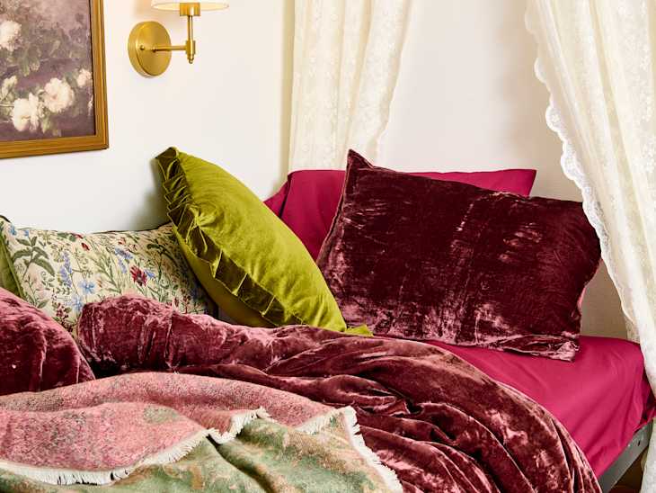 Cozy bed with a mix of colorful pillows, including green velvet and floral patterns, layered with a pink blanket.