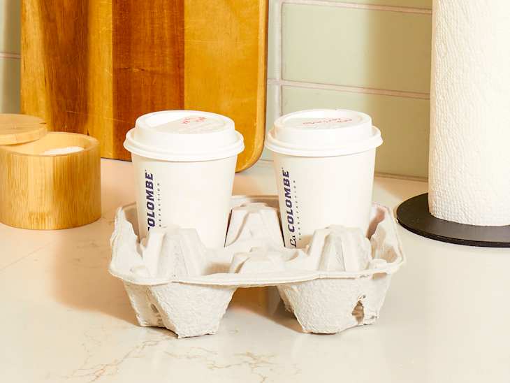 Head on shot of a cardboard drink holder sitting on a white marble counter, holding two cups of coffee.