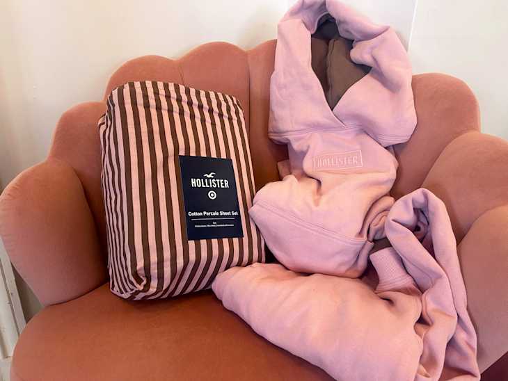 A pink upholstered chair with a striped cotton sheet set and two pink hoodies draped over it.