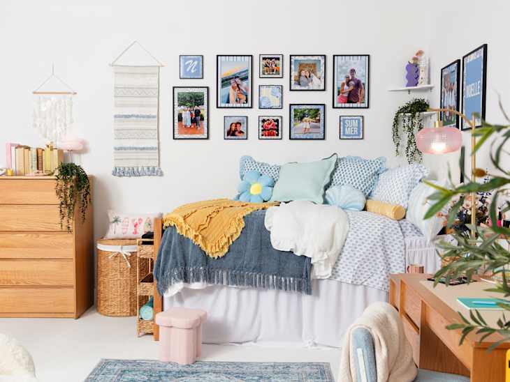 Cozy bedroom featuring a bed with colorful pillows, a wooden dresser, framed photos on the wall, and a pink lamp.