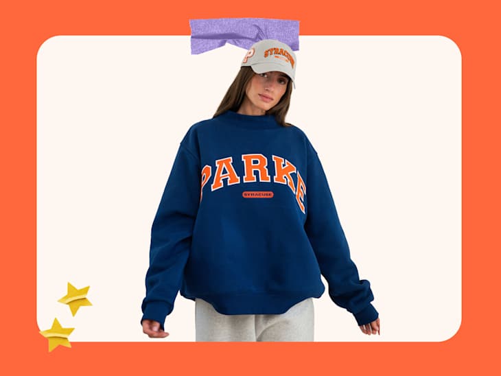 Young woman wearing a navy blue sweatshirt with "PARK" text and a gray cap, posing against a colorful background.