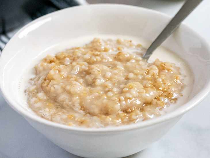 Bowl of oatmeal with milk and a spoon on a light surface.