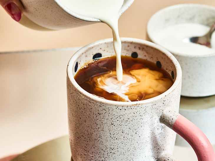 Someone pouring cream into coffee in a ceramic mug