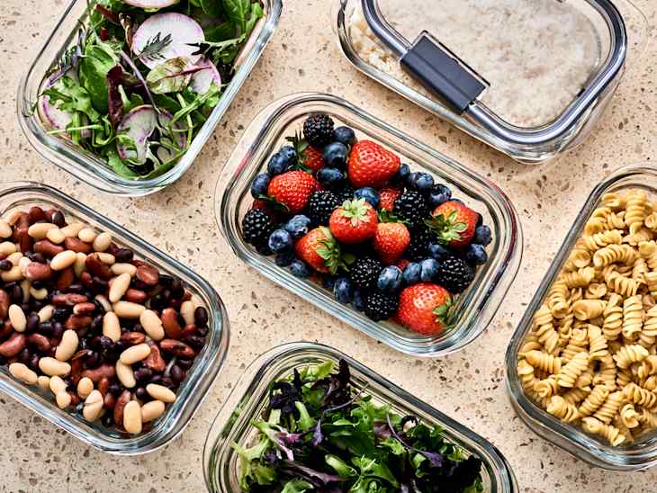 counter with glass containers full of food prep: berries, pasta, salad, beans
