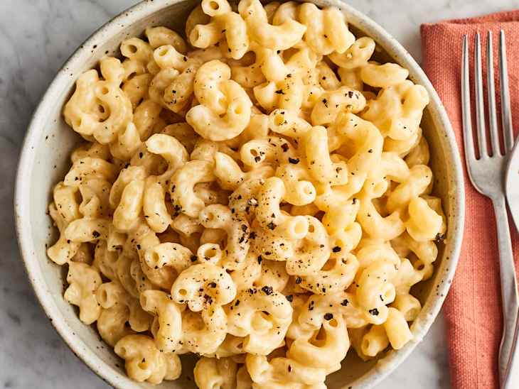 Creamy macaroni and cheese in a bowl, topped with black pepper, next to a pink napkin and fork.