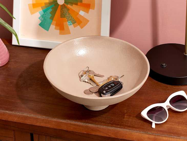 closeup shot of keys in a cream bowl placed on a brown dresser top