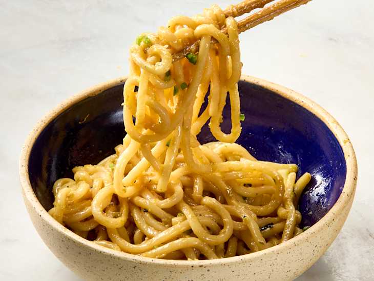 Lemon jalapeno udon noodles being picked up from a bowl with chopsticks.