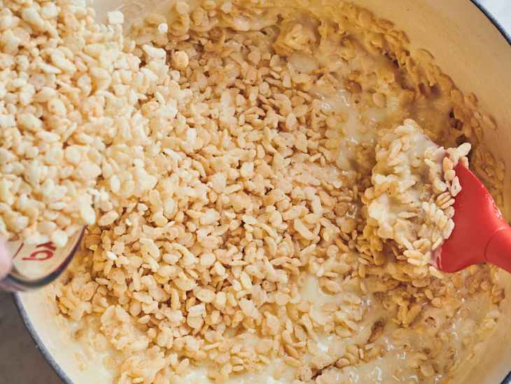 someone is pouring rice krispies into pot with marshmallow and other rice krispies