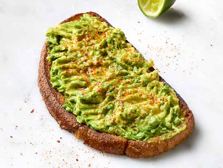 avocado toast on a marble background, sprinkled with Tajin and with a lime wedge squeezed next to it.