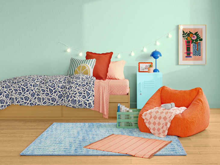 Cozy bedroom with a mint green wall, a bed with patterned bedding, an orange bean bag chair, and decorative string lights.