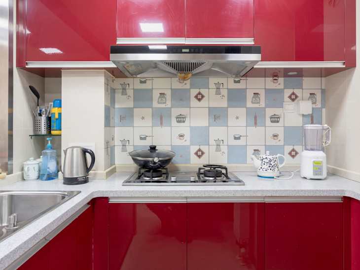 Red kitchen cabinets, gas stove with wok, kettle, blender, and patterned tile backsplash.