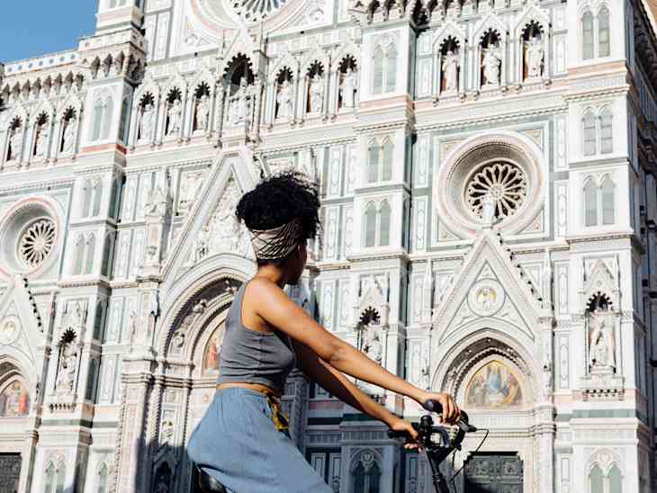 Young woman riding bicycle in front of cathedral, Florence, Italy