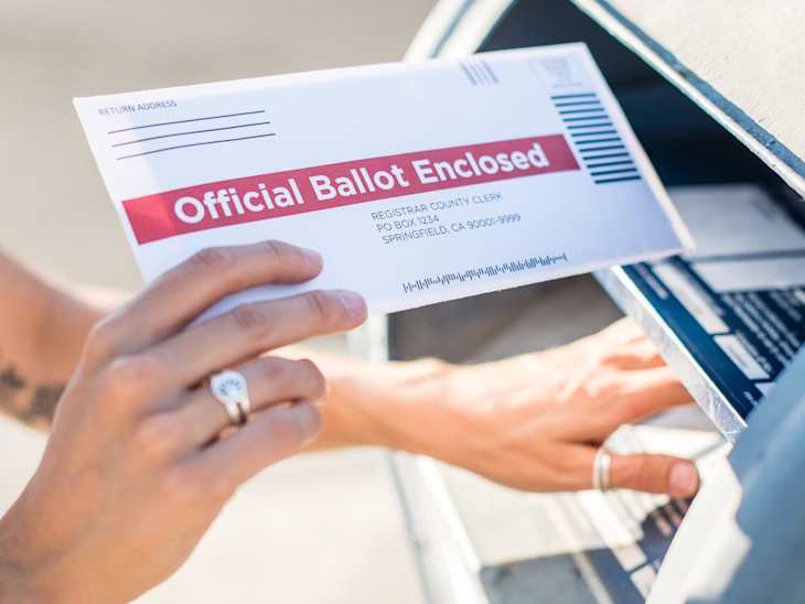A young woman places her absentee voter ballot for the 2020 presidential election into a blue United States Postal mailbox.