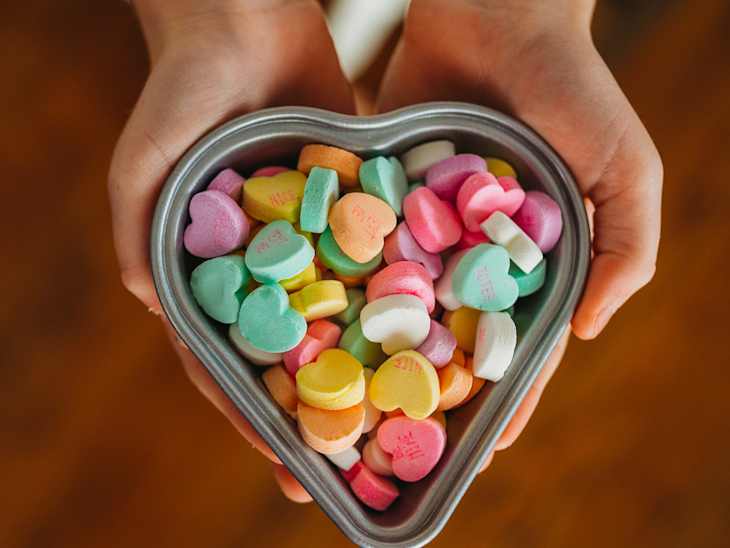 Hands holding a heart-shaped dish of conversation hearts candy