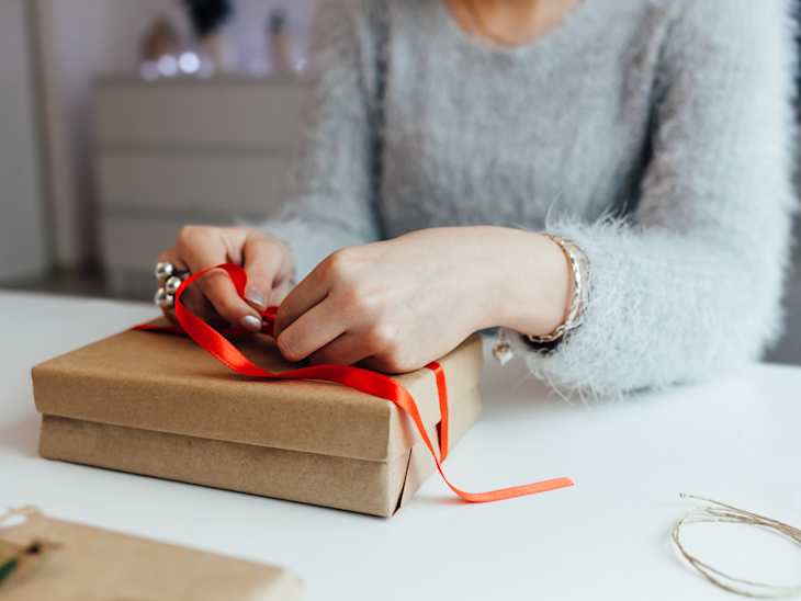 woman wearing gray fuzzy sweater wrapping a gift with red ribbon