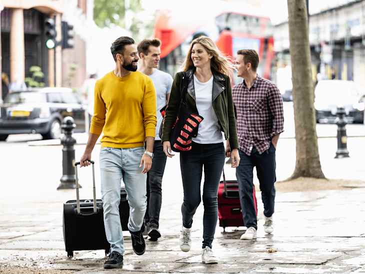 Full length front view of relaxed Indian and Caucasian vacationers in 20s and 30s wearing casual weekend clothing and walking side by side talking.