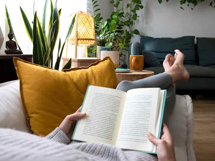 POV of young woman relaxing at home reading a book lying on sofa. Lifesyle concept.