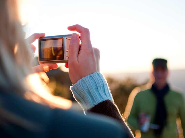 Young female taking a picture of young male with consumer digital camera. The screen shows an image of the subject.