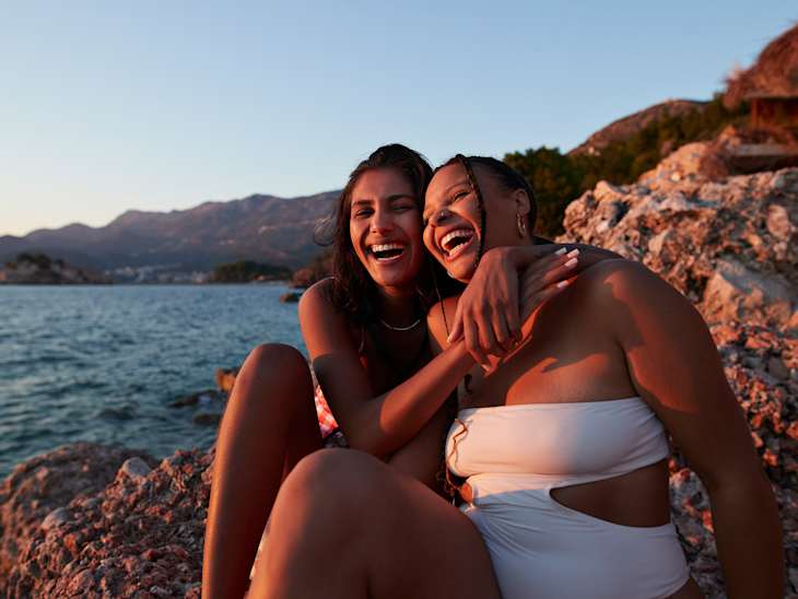 Woman enjoying sunset with friend at rocky beach