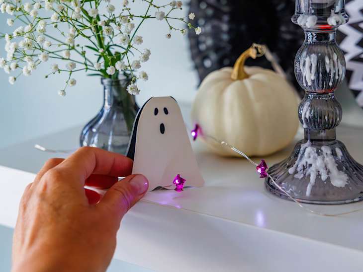 A close-up of a hand placing a ghost paper card on a shelf while decorating a room for Halloween