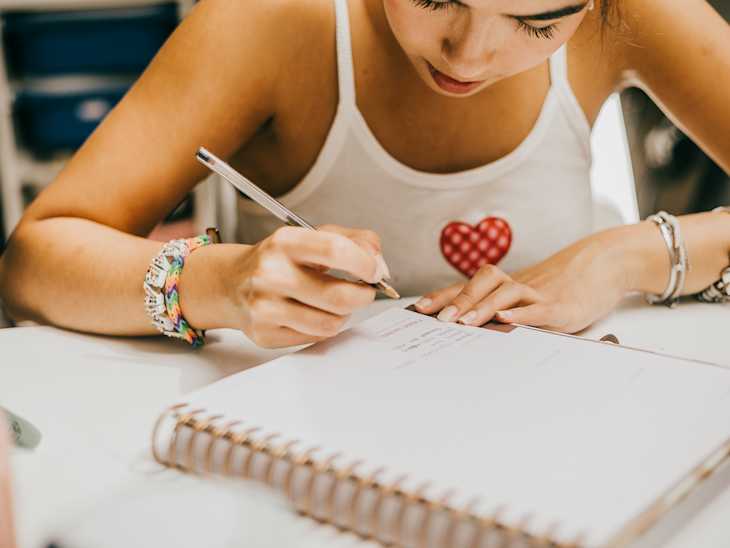 Young woman concentrated as she write in a ruled notebook, possibly for planning, journaling, or note-taking.