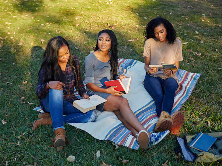 Three friends reading books on a blanket in a park in early Fall
