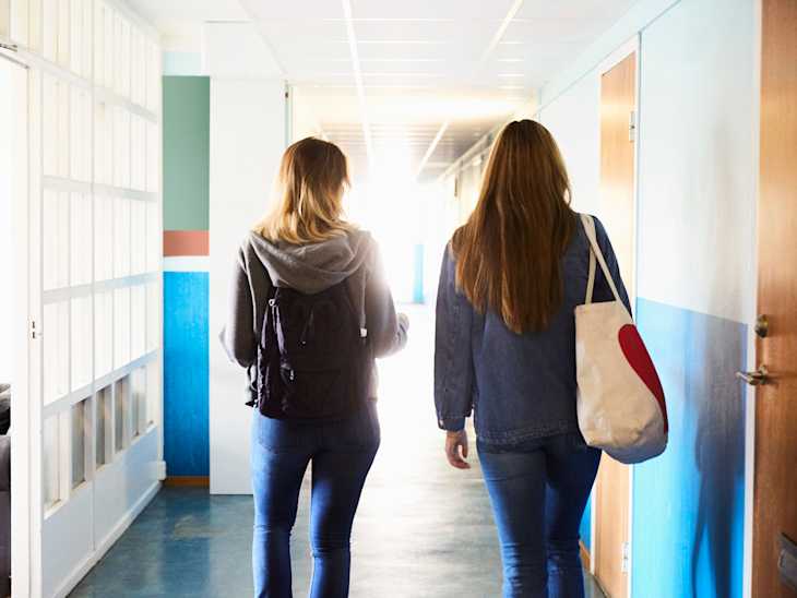 Rear view of friends walking in corridor at university on sunny day