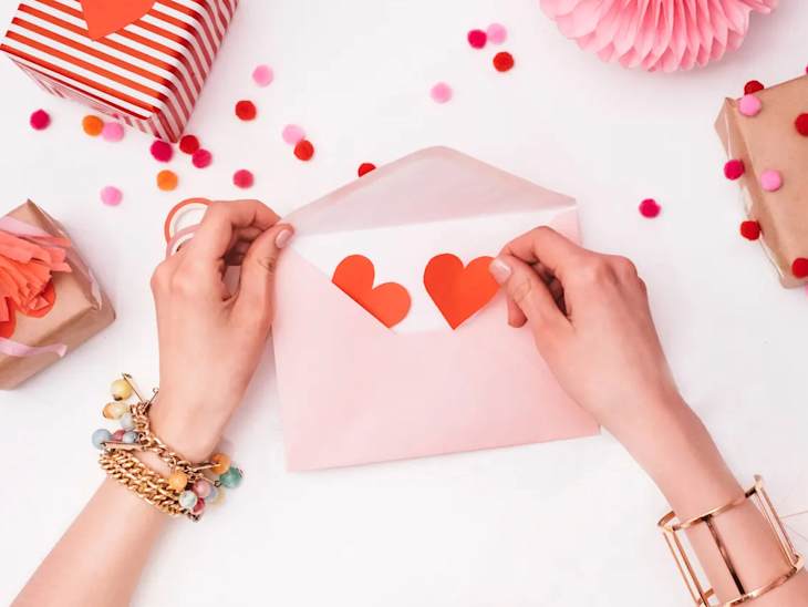 Hands putting hearts in Valentine's Day card envelope.